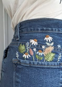 the back of a woman's jeans with daisies and leaves embroidered on it