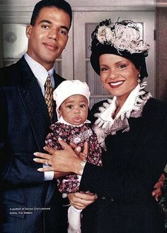 a man standing next to a woman holding a baby in front of her and smiling at the camera