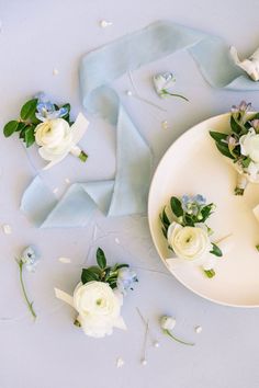 small white flowers are on a plate with blue ribbon and petals scattered around it,