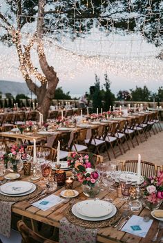 a table set up with place settings and candles for an outdoor wedding reception at dusk