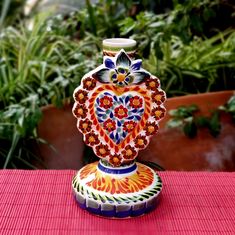 a colorful vase sitting on top of a red table next to potted greenery