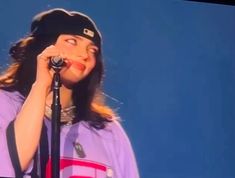 a woman singing into a microphone while wearing a purple shirt and black hat with the word love written on it