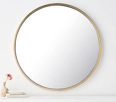 a round mirror sitting on top of a white shelf next to a vase with a flower in it