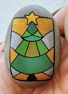 a hand holding a rock with a christmas tree painted on it and another rock in the background