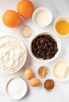 the ingredients for an orange cake are arranged in bowls on a white countertop, including eggs, flour, butter, and raisins