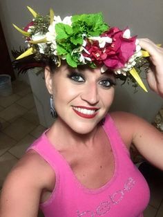 a woman with flowers in her hair smiling at the camera while wearing a pink tank top