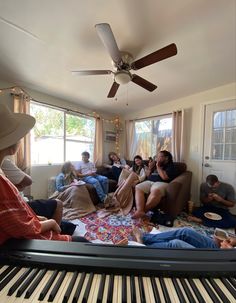 a group of people sitting on couches in a living room with piano and ceiling fan