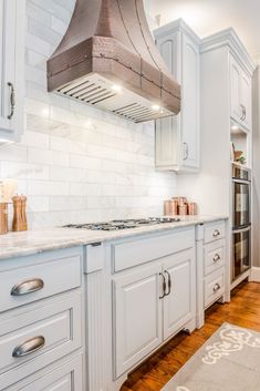 a kitchen with white cabinets and an oven hood in the middle of the countertop