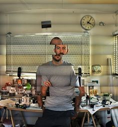 a man standing in front of a desk with a clock on the wall behind him