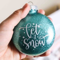 someone holding up a green ornament with the words let it snow on it