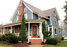 a blue house with red steps and bushes on the front porch is pictured in this image