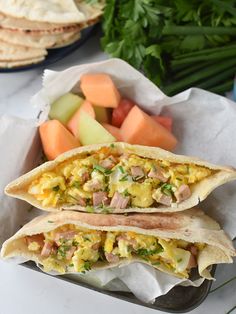 two breakfast burritos with meat, vegetables and fruit on a table next to other foods