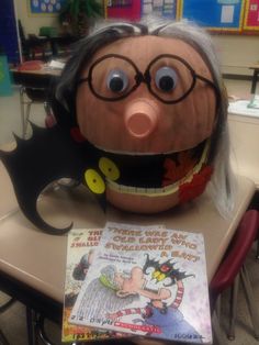 an old woman's head is sitting on a desk with a book in front of it