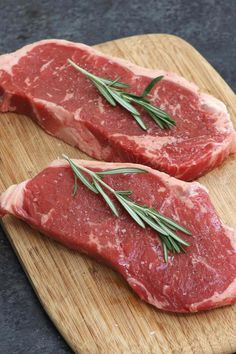 two pieces of raw meat sitting on top of a wooden cutting board