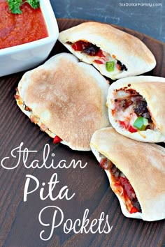 four pita pockets sitting on top of a wooden cutting board next to a bowl of tomato sauce