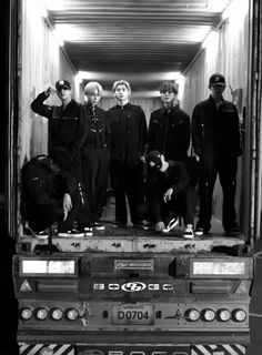 black and white photograph of five men standing on the back of a semi - truck