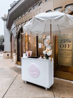 a white cart sitting in front of a store with an umbrella over it's top