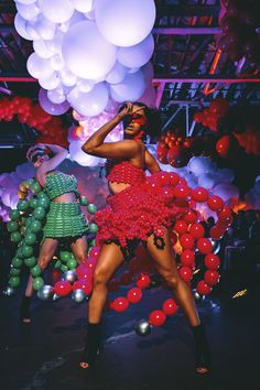 two women dressed in red and green are dancing with balloons on the ceiling behind them