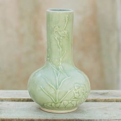 a light green vase sitting on top of a wooden table in front of a wall