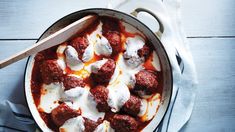 a pot filled with meatballs and sauce on top of a wooden table next to a spoon