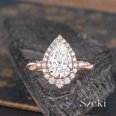 an engagement ring with a pear shaped diamond surrounded by small white pearls on top of a rock