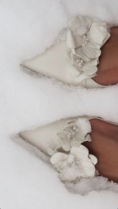 two pairs of white shoes with flowers on them in the snow, side by side