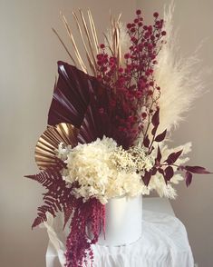 a white vase filled with lots of different types of flowers and plants on top of a table