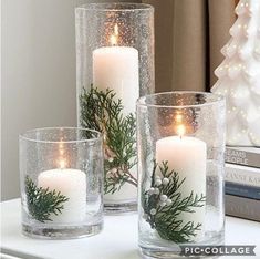 three candles are sitting on a table next to some books and a christmas tree in a vase