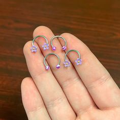 three small purple flowers are in the palm of a person's hand on a wooden table