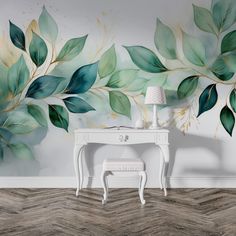 a room with a desk, chair and painted leaves on the wall behind it is a white table