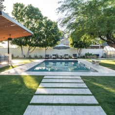 a backyard with a swimming pool, patio and dining area in the back yard is surrounded by trees