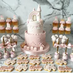 a pink cake surrounded by cupcakes, cookies and other treats on a table