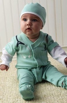 a baby sitting on the floor wearing a green outfit