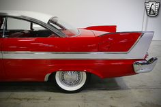 an old red and white car with chrome rims parked in a garage next to a wall