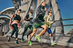 four people are running on a bridge in the city, one is wearing green and the other is black