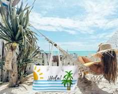 a woman sitting in a hammock on the beach with a bag hanging from it