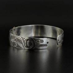 "This is a new, handmade Northwest Coast First Nations cuff bracelet. Depicting the 'Raven Stealing the Sun', this cuff measures 1/2\" wide by 6\" long. It will fit a wrist between 6 1/4\" - 6 3/4\" in circumference, and its shape can be altered. It is made from sterling silver, and then a hand-carved and hand-filed solid 14k gold overlay is laboriously soldered on top by designer Kelvin Thompson. It is signed on the inside. Note each cuff is unique and will be slightly different. The 'Raven' is Symbolic Engraved Cuff Bangle Bracelet, Engraved Sterling Silver Cuff Bracelet For Ceremonial Occasions, Symbolic Stamped Cuff Bracelet, Sterling Silver Engraved Cuff Bracelet For Ceremonial Wear, Symbolic Engraved Ceremonial Cuff Bracelet, Symbolic Engraved Cuff Bracelet For Ceremonies, Ceremonial Polished Cuff Bangle Bracelet, Ceremonial Bangle Cuff Bracelet With Polished Finish, Symbolic Stamped Cuff Bangle Bracelet