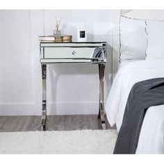 a mirrored nightstand table in a bedroom with a white bed and gray rug on the floor