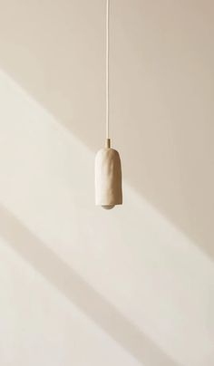 a white light hanging from a ceiling in a room with beige walls and shadows on the wall