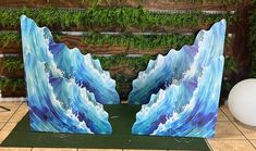 two pieces of art that look like waves in blue and white paint on green paper