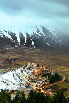 an aerial view of a small village in the mountains with snow on it's tops