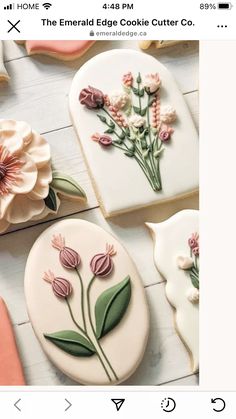 some cookies decorated with flowers and leaves on top of a white table next to cookie cutters