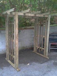 two wooden structures sitting in the middle of a parking lot next to a wall and trees