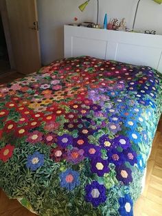 a bed covered in a multicolored crocheted blanket with flowers on it