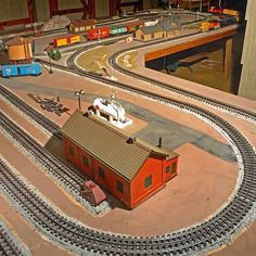 a model train track with a small red building on the top and a blue car in the middle