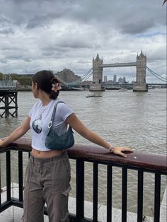 a woman standing on a bridge looking out over the water with a city in the background