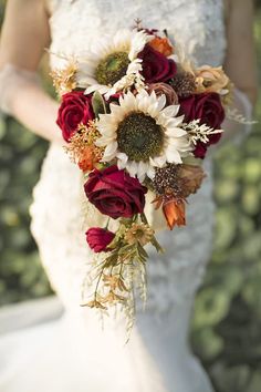 a bride holding a bouquet of sunflowers and red roses in her wedding dress