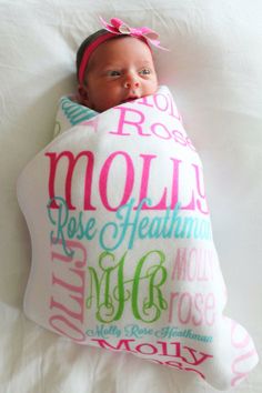 a baby wrapped in a blanket on top of a white bed with pink and green lettering