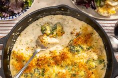 a skillet filled with broccoli and cheese on top of a table next to salad