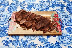 sliced beef on a wooden cutting board with blue floral table cloth and red flowered napkin